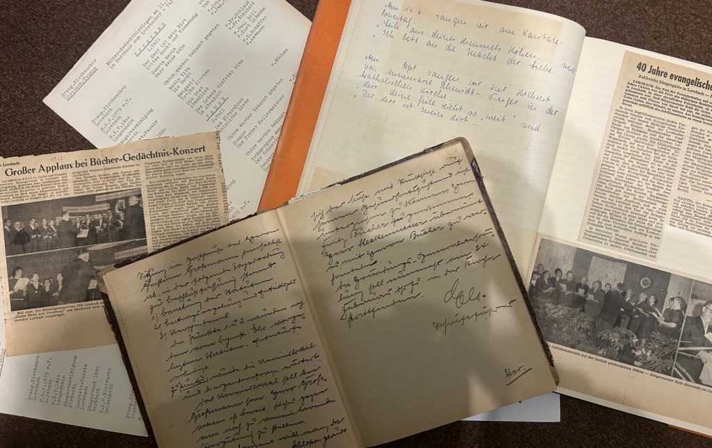 Fotografie historischer Dokumente und Zeitungsausschnitte zur Chorgeschichte Lorsbachs, darunter handschriftliche Notizen, Konzertprogramme und Presseartikel.